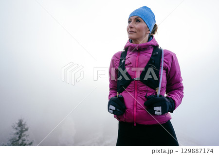 Confident female hiker in a pink jacket standing still on a misty mountain summit.Female Hiker Standing on Misty Peak Confident female hiker in a pink jacket standing still on a misty mountain summit.Female Hiker Standing on Misty Peak 129887174