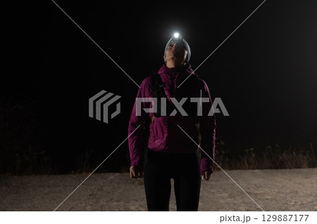 Woman Jogging at Night with Headlamp.Woman jogging at night with headlamp on, captured in dark outdoor environment. 129887177