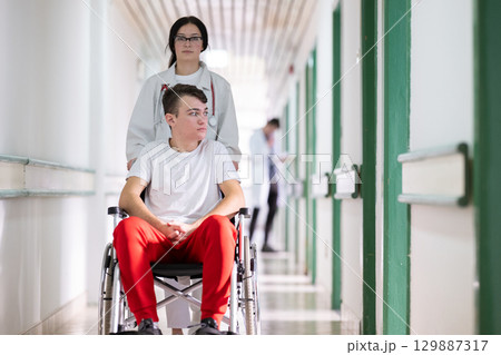Young Male Patient in Wheelchair Assisted by Female Medical Professional Young Male Patient in Wheelchair Assisted by Female Medical Professional 129887317