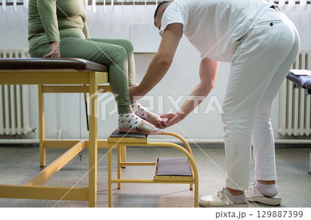 Physical Therapist Assisting Elderly Patient.Physiotherapist helping an elderly woman with leg movement on a step platform during a rehabilitation session. Physical Therapist Assisting Elderly Patient.Physiotherapist helping an elderly woman with leg movement on a step platform during a rehabilitation session. 129887399
