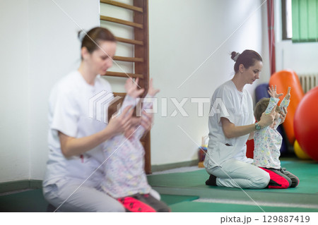 Pediatric Physiotherapy Session.Female physiotherapist helping a young child with physical exercises in a rehabilitation center. Pediatric therapy and development concept. 129887419