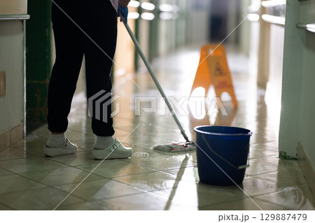 Cleaning Staff in Hospital Hallway.Female janitor standing in a hospital corridor with mop and bucket, symbolizing cleanliness and hygiene. 129887479