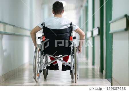 Young teenage boy smiling while sitting in a wheelchair in a hospital hallway. Rehabilitation and positivity concept. Young teenage boy smiling while sitting in a wheelchair in a hospital hallway. Rehabilitation and positivity concept. 129887488