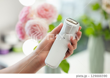 Tool for facial massage in hand of a professional cosmetologist, close up, flowers on the background. Professional device for body and skin care concept Tool for facial massage in hand of a professional cosmetologist, close up, flowers on the background. Professional device for body and skin care concept 129888390