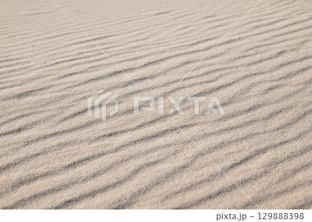 Sand beach with waves. Close up of sand under bright sunlight, wind made waves on it 129888398