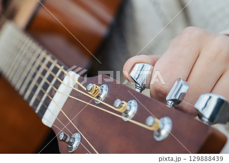 Changing guitar strings close up, tuning new strings of an acoustic guitar. Female musician tuning guitar, close up shot 129888439