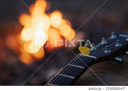 Close up on yellow mediator on guitar with bonfire on the background. Playing guitar, music, having good time camping on nature 129888447