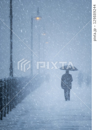 person walking with umbrella through snowstorm 129889244