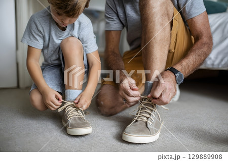 dad tying shoelaces for boy preparing for school morning 129889908