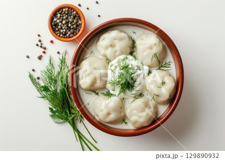 Dumplings with fresh dill and cream in brown bowl, isolated on solid white background. Peppercorns scattered nearby. Top view. Neural network AI generated 129890932