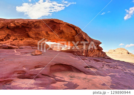 Little arc or small rock window formation in Wadi Rum desert, bright sun shines on red dust and rocks, blue sky above Little arc or small rock window formation in Wadi Rum desert, bright sun shines on red dust and rocks, blue sky above 129890944