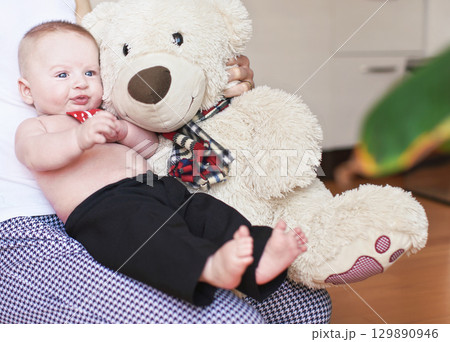 Four months old baby boy sitting on her mother knees, large plush teddy bear next to him Four months old baby boy sitting on her mother knees, large plush teddy bear next to him 129890946