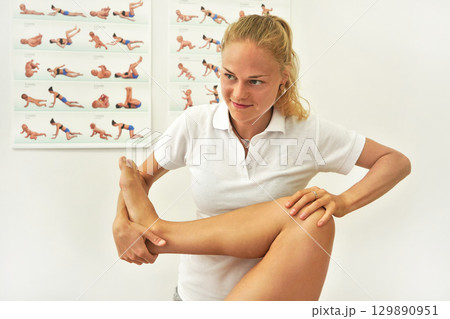 Young female physiotherapist exercising with her patient, flexing her knee muscles Young female physiotherapist exercising with her patient, flexing her knee muscles 129890951