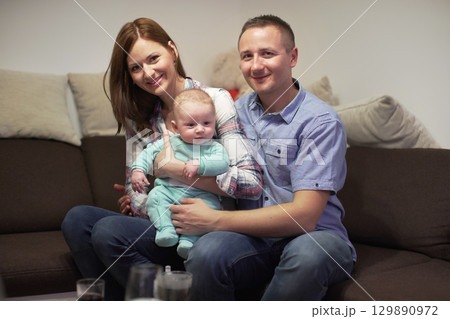 Young couple sitting on couch with his 3 months old baby boy, posing for family photo Young couple sitting on couch with his 3 months old baby boy, posing for family photo 129890972