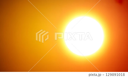 Bright glowing sun with halo effect against gradient orange background capturing radiant solar energy 129891018