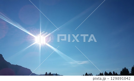Sun flare in blue sky above mountain and tree silhouettes on sunny day 129891042