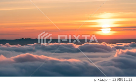 Aerial view of clouds with a sunset sky and distant land silhouette seen 129891112