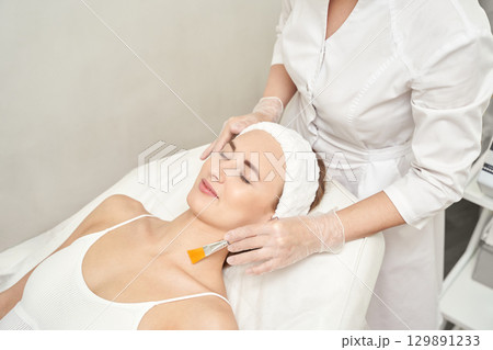 Young caucasian female relaxing during facial treatment at beauty spa clinic 129891233