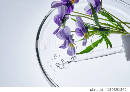 A drop of serum and a pipette with pansies in close-up. 129891262