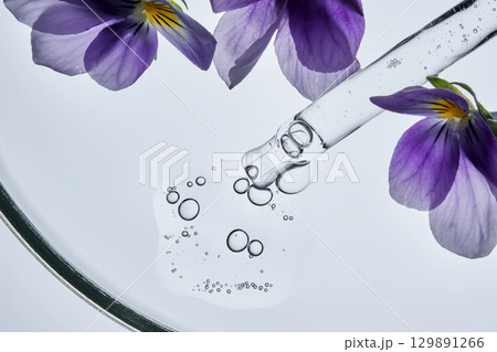 A drop of serum and a pipette with pansies in close-up. 129891266