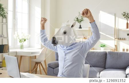 Funny extravagant happy man wearing donkey, horse head happy celebrating near laptop online 129891352