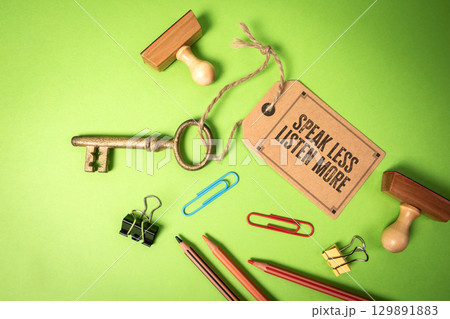 Golden Key With Tag Message Speak Less, Listen More on Green Background With Office Supplies 129891883