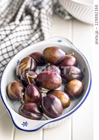 Ripe plums in bowl on white table. 129892168
