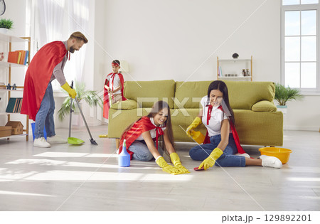 Cheerful parents and children in superhero costumes are cleaning house together. Cheerful parents and children in superhero costumes are cleaning house together. 129892201