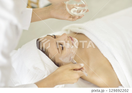 Young woman enjoying facial mask during professional skin care procedures at spa salon 129892202