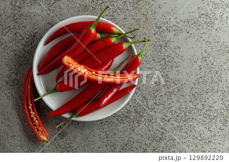 Fresh red chili peppers with green stems on a gray stone table. 129892220