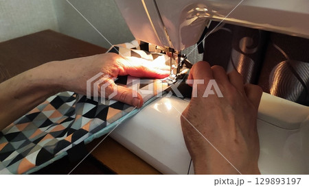 Close-up of hands sewing patterned fabric on a sewing machine. craft, tailoring, handmade textile work, DIY fashion and home decor. 129893197