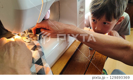 Child watching sewing on machine - DIY crafting, family bonding, handmade textiles, slow living home studio, sustainable fashion learning moment 129893369