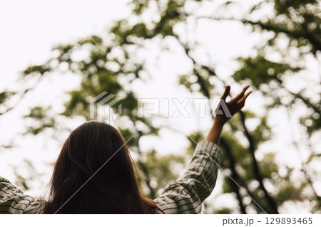 Woman embracing nature in forest back view with arms raised, enjoying the inner peace, harmony and freedom. Human and nature connection. Woman embracing nature in forest back view with arms raised, enjoying the inner peace, harmony and freedom. Human and nature connection. 129893465