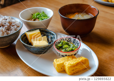 雑穀ご飯や味噌汁、卵焼きと小鉢が並ぶ和風の朝食セット 129893822