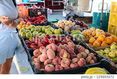 Diverse fresh fruits and vegetables displayed at a vibrant outdoor market, promoting healthy eating habits and local produce. A shopper explores the colorful and inviting selection available. Diverse fresh fruits and vegetables displayed at a vibrant outdoor market, promoting healthy eating habits and local produce. A shopper explores the colorful and inviting selection available. 129893872