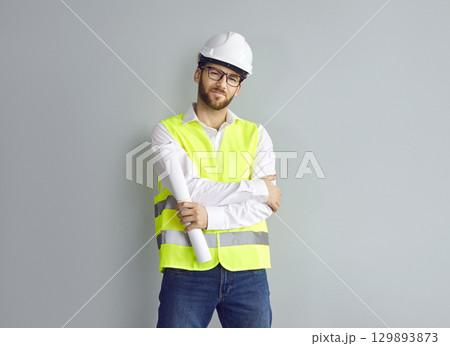 Male architect, builder or construction engineer in uniform and hard hat standing by house wall Male architect, builder or construction engineer in uniform and hard hat standing by house wall 129893873