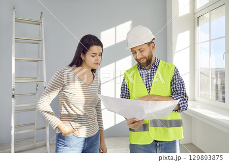 Builder or architect talking to a young woman and showing her the construction plan Builder or architect talking to a young woman and showing her the construction plan 129893875