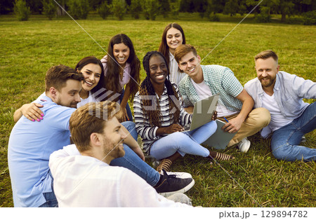 University friends working and studying together using laptop while sitting on grass of campus park. University friends working and studying together using laptop while sitting on grass of campus park. 129894782