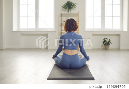 Yogi girl in yoga lotus pose rear view, slim woman practicing yoga or working out, wearing sport wear indoor Yogi girl in yoga lotus pose rear view, slim woman practicing yoga or working out, wearing sport wear indoor 129894795