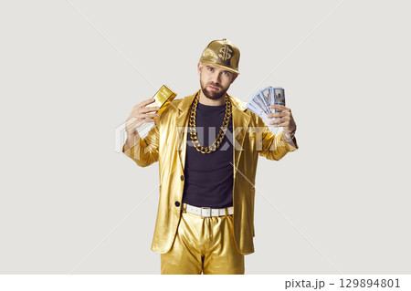 Funny man in golden suit holding money cash and gold bar on white studio background. Funny man in golden suit holding money cash and gold bar on white studio background. 129894801