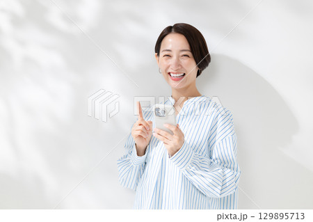 木漏れ日の中でスマホを持つ女性 129895713