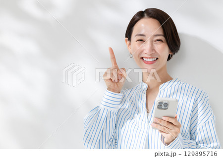 木漏れ日の中でスマホを持つ女性 木漏れ日の中でスマホを持つ女性 129895716