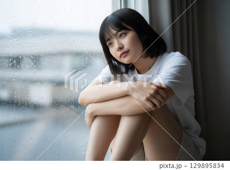 雨の日の窓辺で過ごす女性のポートレート 129895834