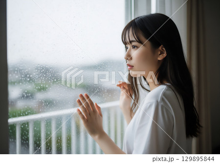 雨の日の窓辺で過ごす女性のポートレート 129895844