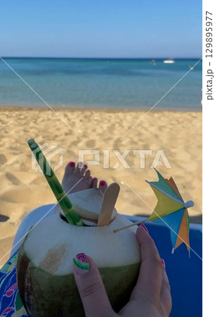 Tropical coconut drink with umbrella on sandy beach by the sea Tropical coconut drink with umbrella on sandy beach by the sea 129895977