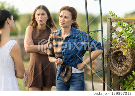 Three women arguing in cottage garden 129897012