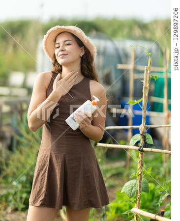 Young woman applying sunscreen in cottage garden 129897206