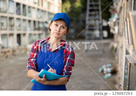 Female cemetery employee stands with report and writes down information. Female cemetery employee stands with report and writes down information. 129897263