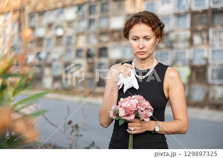 Sorrowful woman in black standing in cemetery with flowers Sorrowful woman in black standing in cemetery with flowers 129897325
