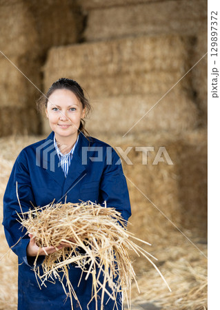 Cheerful woman farmer holding bunch of hay Cheerful woman farmer holding bunch of hay 129897372